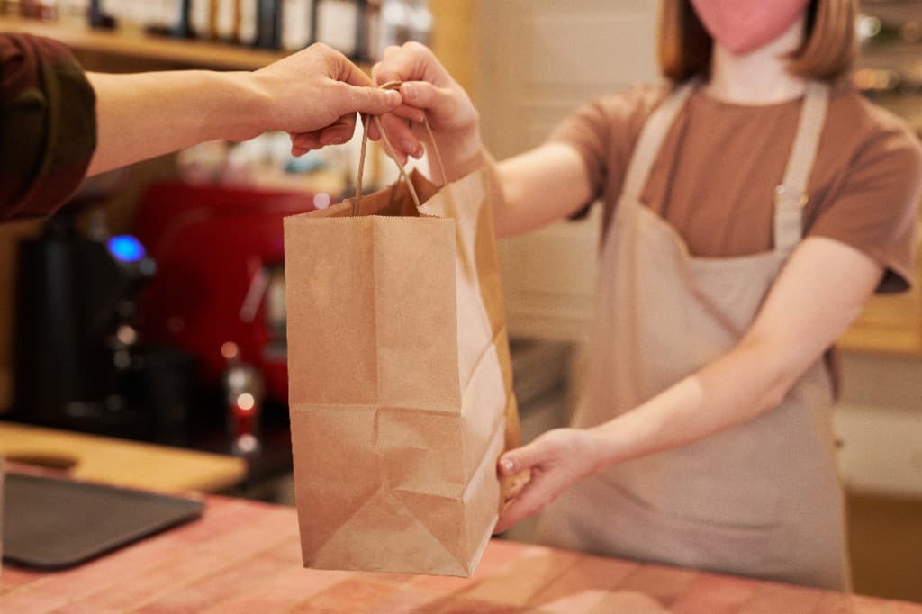 En ansatt overleverer en takeaway-pose til en kunde over disken